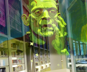 A large, green - painted sculpture of a man with a book in his hand.
(city, exhibition, street, glass items, business, urban, art, mannequin, light, architecture, downtown, travel, shopping, neon, futuristic, contemporary, design, fashion, stock, window)